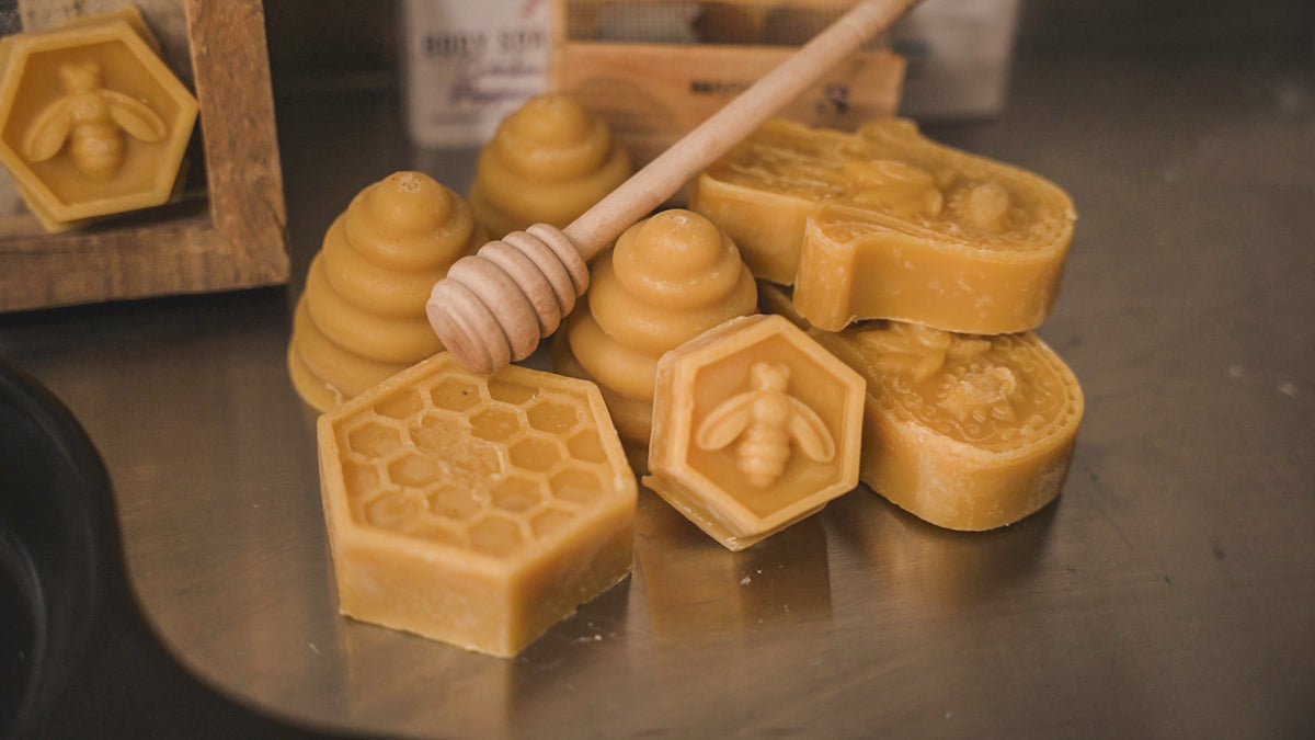 Several yellow beeswax bricks with a honey dipper, on a metal surface with a honeycomb pattern in the background.