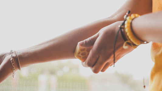 A person is holding a lotion bar up to their arm, applying it to their skin. They are wearing a yellow top and have bracelets on their wrist.