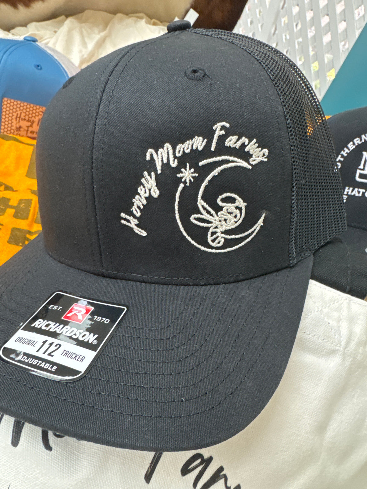 Black cap with white Honey Moon Farms embroidery on a textured surface