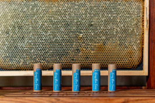 five tubes of organic lip balm with blue caps, placed in front of a honeycomb background.