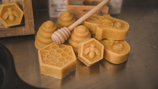 Several yellow beeswax bricks with a honey dipper, on a metal surface with a honeycomb pattern in the background.