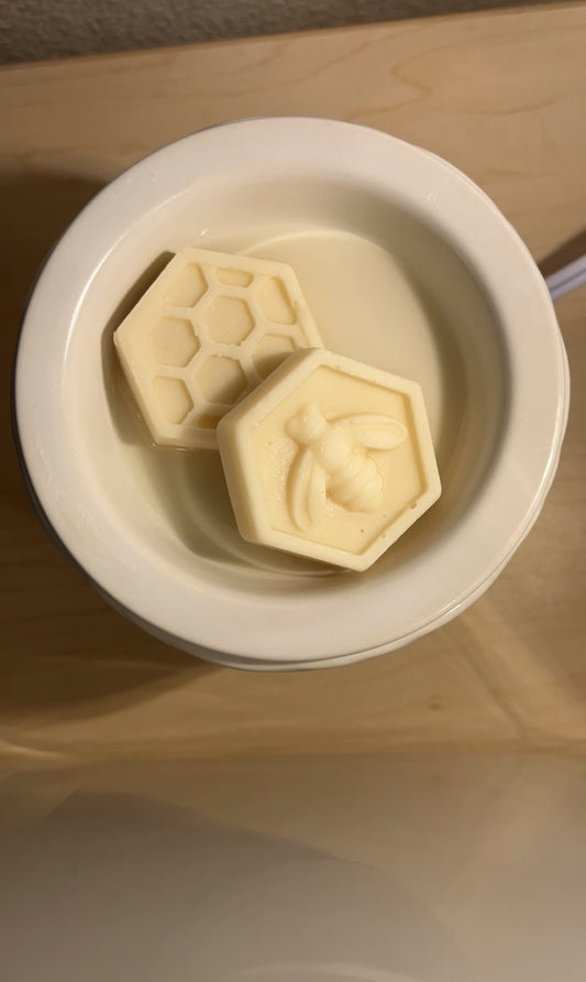 A white ceramic wax warmer dish containing several off-white wax melts, with a honeycomb pattern on the top surface of the dish.